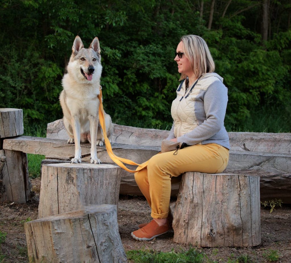 Žena sedící se svou fenkou československého vlčáka venku na dřevěných špalcích.