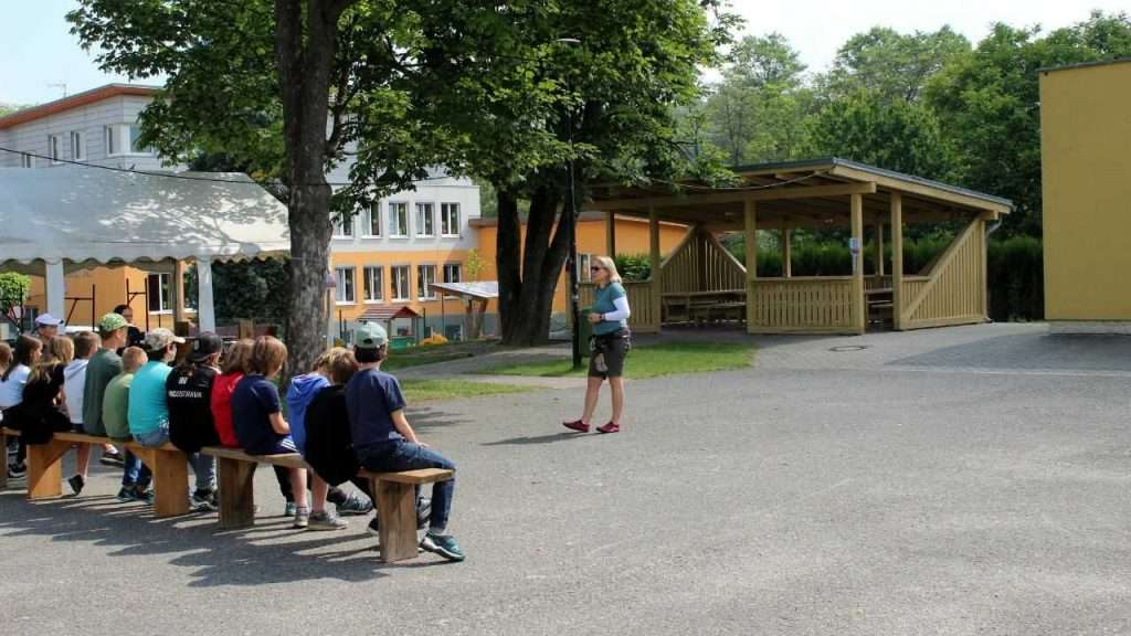 Žena přednáší dětem venku na lavičce.
